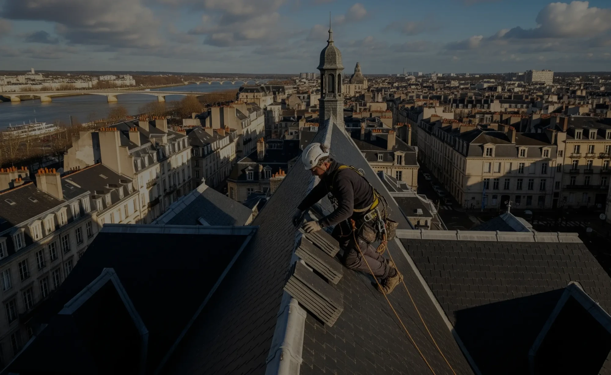Un couvreur professionnel à Nantes travaillant sur un toit en ardoise avec la ville et la Loire en arrière-plan.